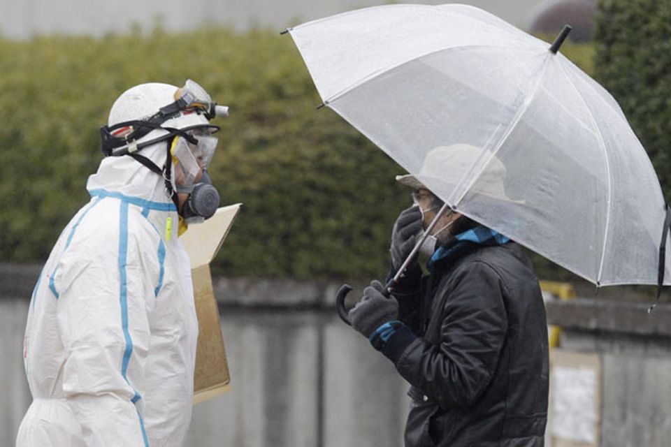 An official wearing a protective suit helps usher people through a radiation emergency scanning center in Koriyama, Japan, Tuesday, March 15, 2011, four days after a giant quake and tsunami struck the country's northeastern coast. (AP Photo/Mark Baker)