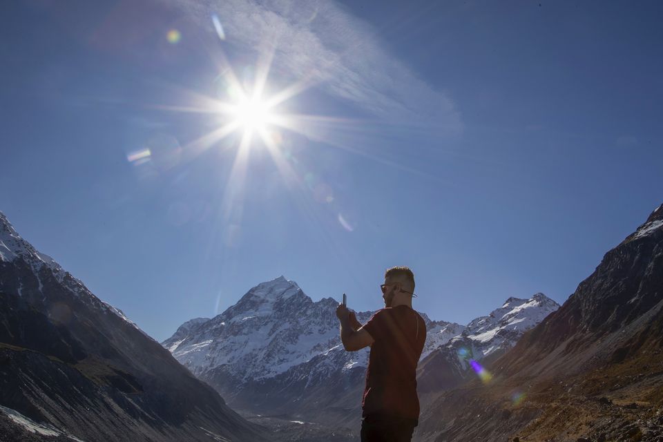 A tourist takes a photo at a frozen lake at the foot of New Zealand’s highest peak, Aoraki, in the Aoraki/Mount Cook National Park (Mark Baker/AP)