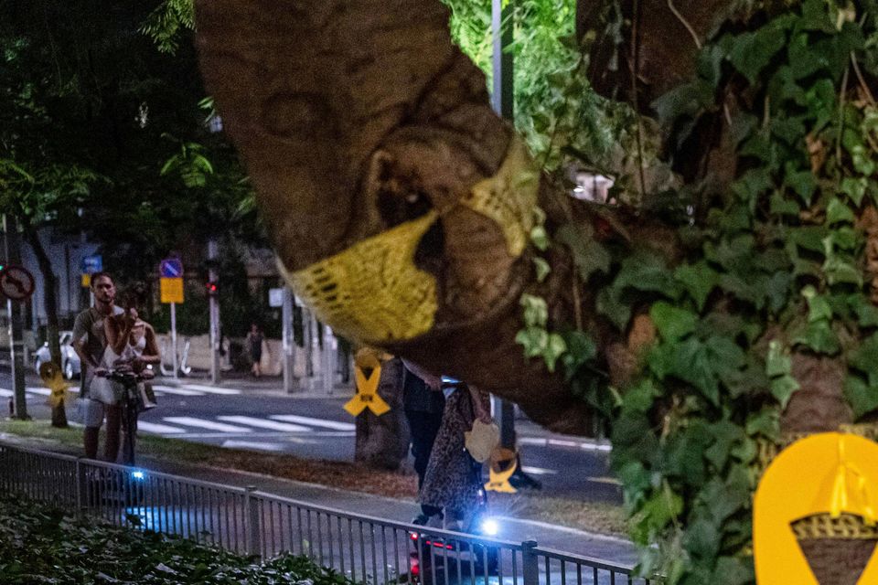 A couple rides a bicycle near a yellow ribbon sign calling for the release of hostages (AP Photo/Ohad Zwigenberg)