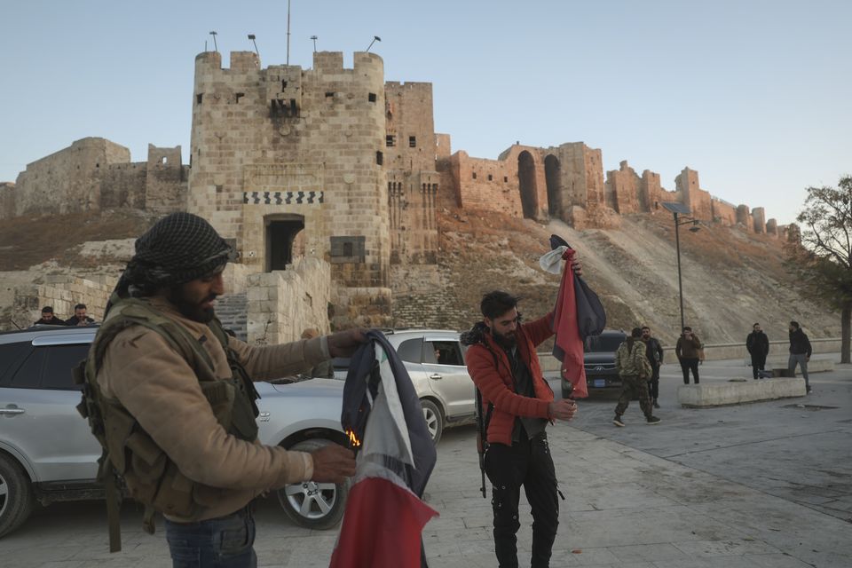 Syrian opposition fighters burn government Syrian flags for the cameras next to Aleppo’s old city (Ghaith Alsayed/AP)