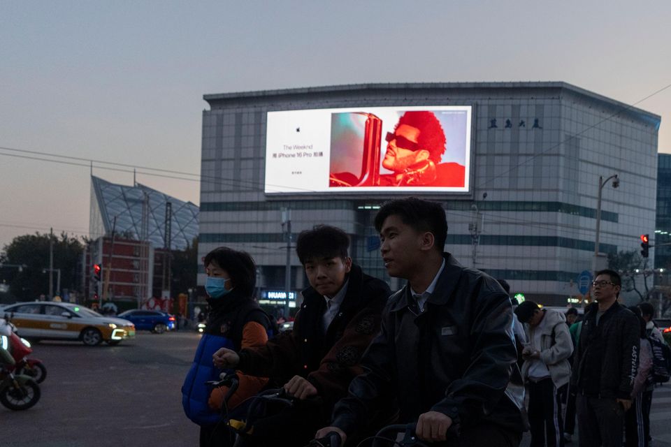 Pedestrians and cyclists wait to cross a traffic junction near a advertisement for iPhones in Beijing (Ng Han Guan/AP)