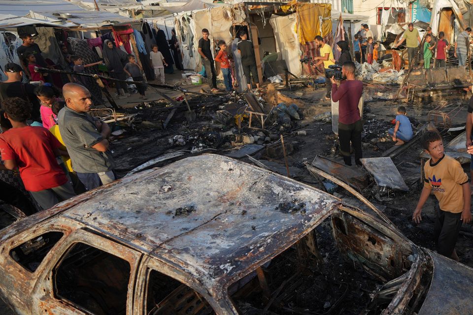 Palestinians look at a burnt-out car after an Israeli strike in Deir al Balah in the Gaza Strip on Monday (Abdel Kareem Hana/AP)