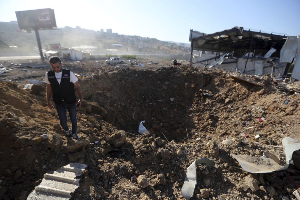 A Lebanese police intelligence officer stands near a crater at the site of an Israeli airstrike that hit a hangar in the southern town of Jiyeh, Lebanon, on Wednesday (Mohammed Zaatari/AP)