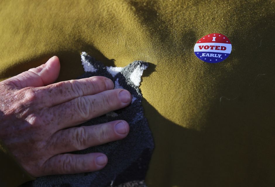 Minneapolis voter Scott Graham touches his heart while wearing an early voting sticker as he is interviewed at the City of Minneapolis early voting centre (Adam Bettcher/AP)