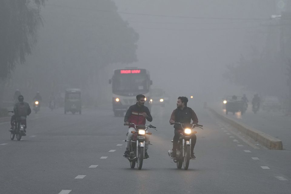 Vehicles and motorcyclists travel with headlights on due to reduced visibility caused by smog in Lahore, Pakistan (KM Chaudary/AP)