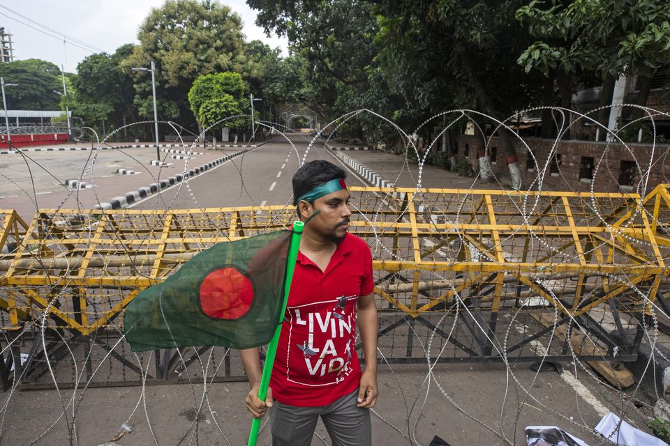 A protester carries the Bangladesh flag as he and others block the road in front of the former residence of Sheikh Mujibur Rahman (Rajib Dhar/AP/PA)