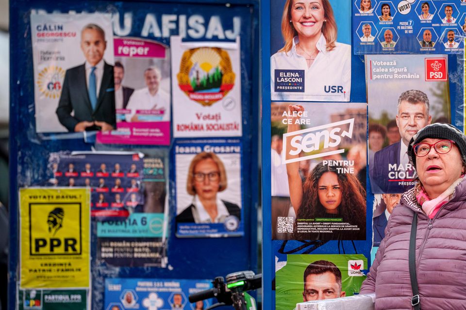 A woman stands by panels displaying electoral posters ahead of the November 24 presidential elections (Andreea Alexandru/AP)