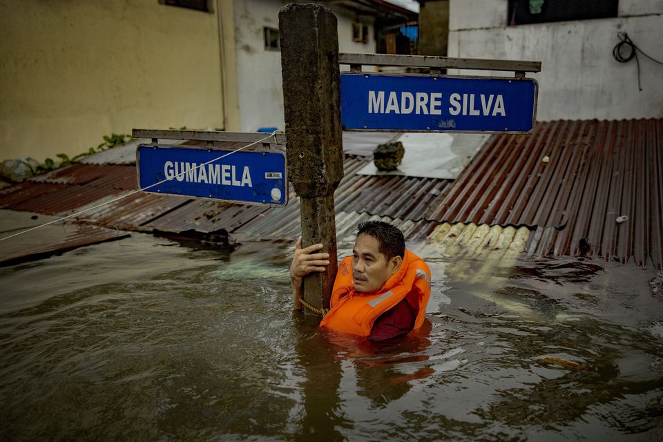 A resident holds on to a street sign in a road flooded by Typhoon Gaemi and monsoon rains on July 24, 2024 in Quezon city, Metro Manila, Philippines. Monsoon rains, intensified by Typhoon Gaemi, have caused flooding and landslides throughout the Philippines, resulting in at least eight deaths and displacing over 600,000 people. (Photo by Ezra Acayan/Getty Images)