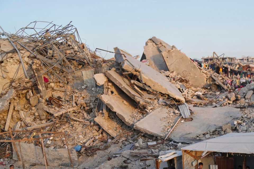 Palestinians walk amid the rubble of destroyed homes and buildings (Jehad Alshrafi/AP)