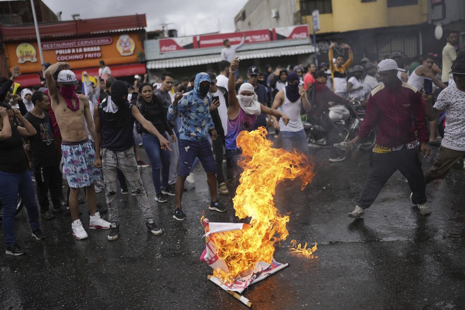 Protesters burn an election campaign poster of President Nicolas Maduro as they demonstrate against the official election results (Matias Delacroix/AP)