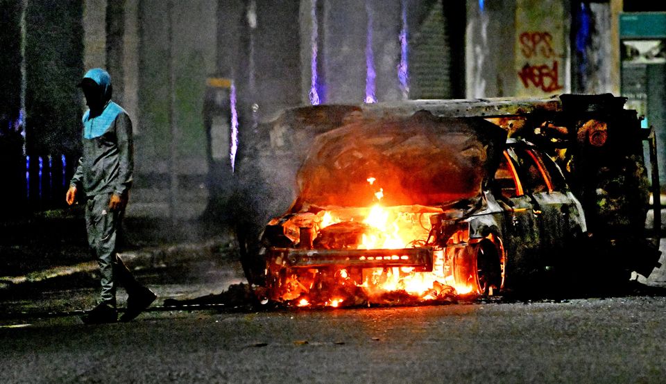 Masked rioter near a burning car