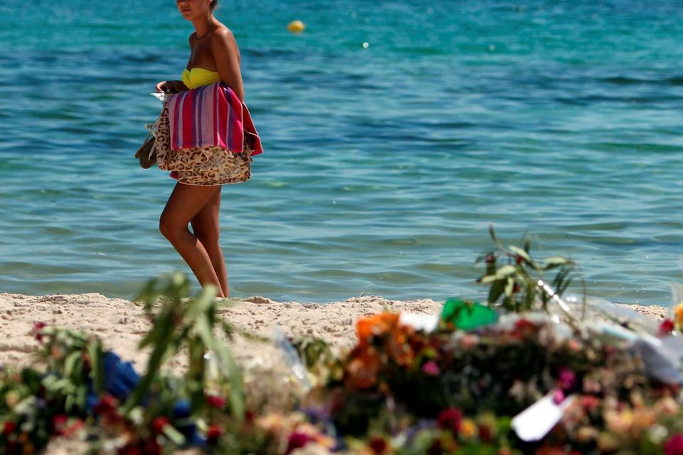 Tourists look at flowers that have been laid on the beach near the RIU Imperial Marhaba hotel in Sousse, Tunisia, as British holidaymakers defy the terrorists and continue to stay in Sousse despite the bloodbath on the beach. PRESS ASSOCIATION Photo. Picture date: Tuesday June 30, 2015. The sands at Sousse were quiet and calm today as tourists and locals alike continued to pay their respects to the 38 dead outside the RIU Imperial Marhaba and Bellevue hotels. Flowers continue to be laid at three heart-shaped memorials that mark where so many people lost their lives, with many people in tears as theyy read the messages of support in several languages that have been placed in the sand. See PA story POLICE Tunisia Tourists. Photo credit should read: Steve Parsons/PA Wire