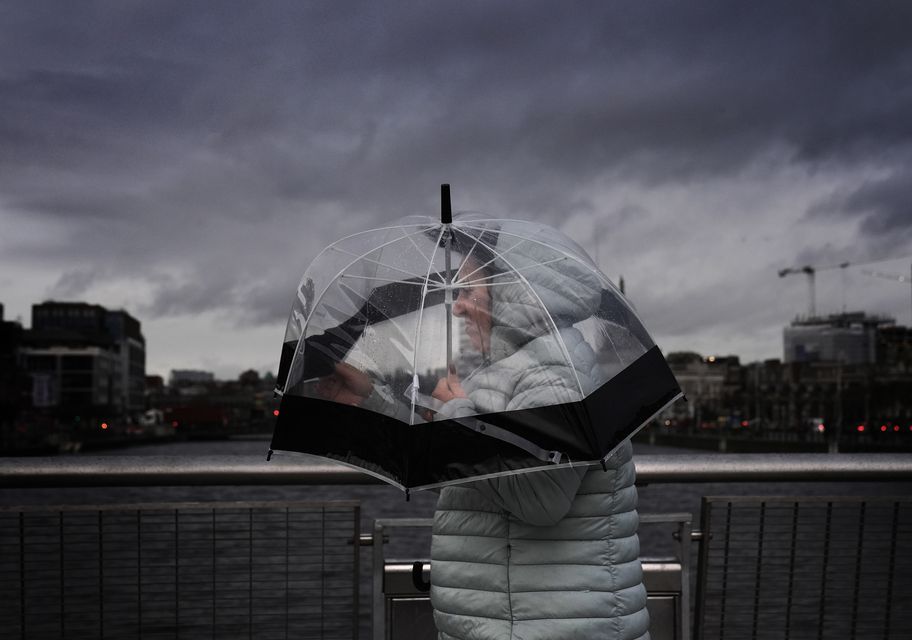 A person takes shelter under an umbrella as they cross the Sean O’Casey Bridge in Dublin’s city centre ahead of Storm Darragh (Brian Lawless/PA)