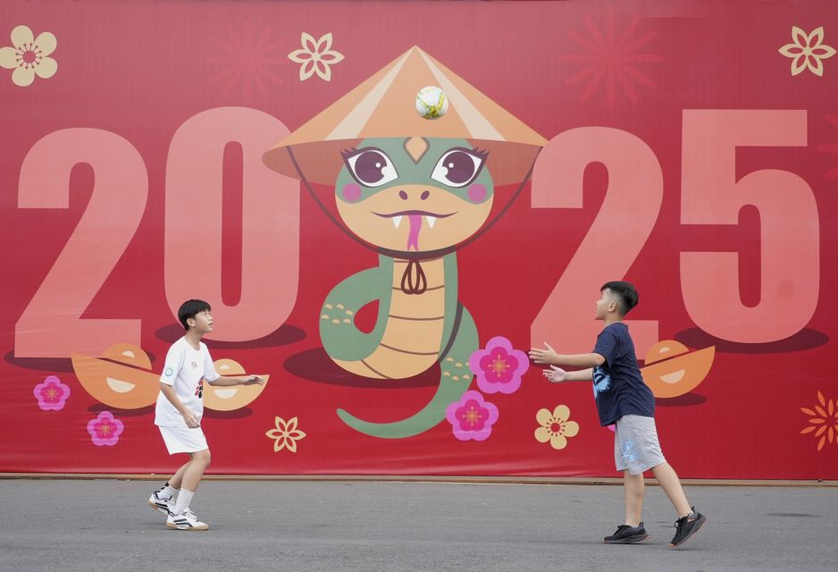 Two boys play football in front of a billboard welcoming the new year 2025 in Ho Chi Minh city, Vietnam (Hau Dinh/AP)