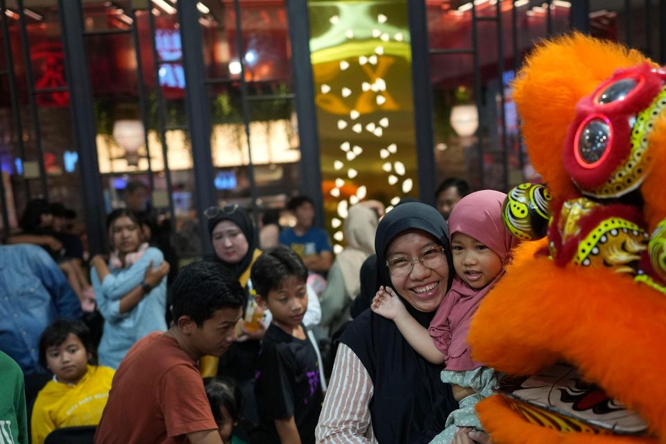 A woman and her daughter have their photo taken with members of dragon dance club Naga Merah Putih in the lion costume (Dita Alangkara/AP)