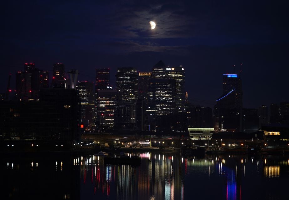 A lunar eclipse is visible above Canary Wharf in London as the full moon passes into Earth’s shadow (Yui Mok/PA)