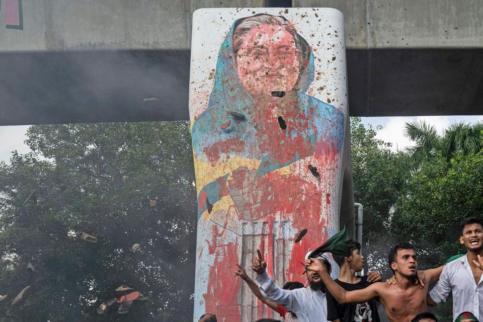 Protesters celebrate beside a defaced portrait of Prime Minister Sheikh Hasina after news of her resignation, in Dhaka, Bangladesh (Fatima Tuj Johora/AP)