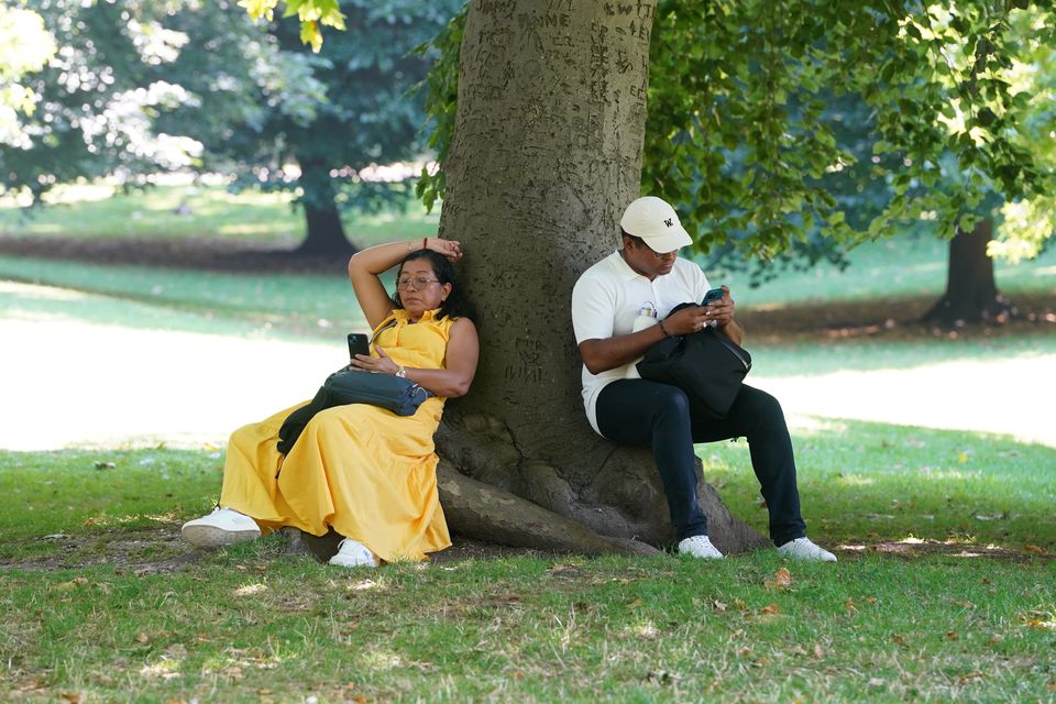 People sit in the shade beneath a tree during hot weather in St James’s Park, central London (Lucy North/PA)