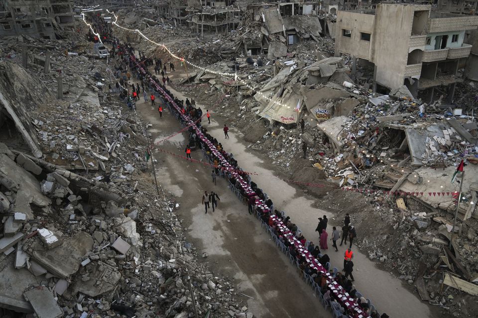 Palestinians sit at a large table surrounded by the rubble of destroyed homes and buildings as they gather for iftar, the fast-breaking meal, on the first day of Ramadan in Rafah (Abdel Kareem Hana/AP)