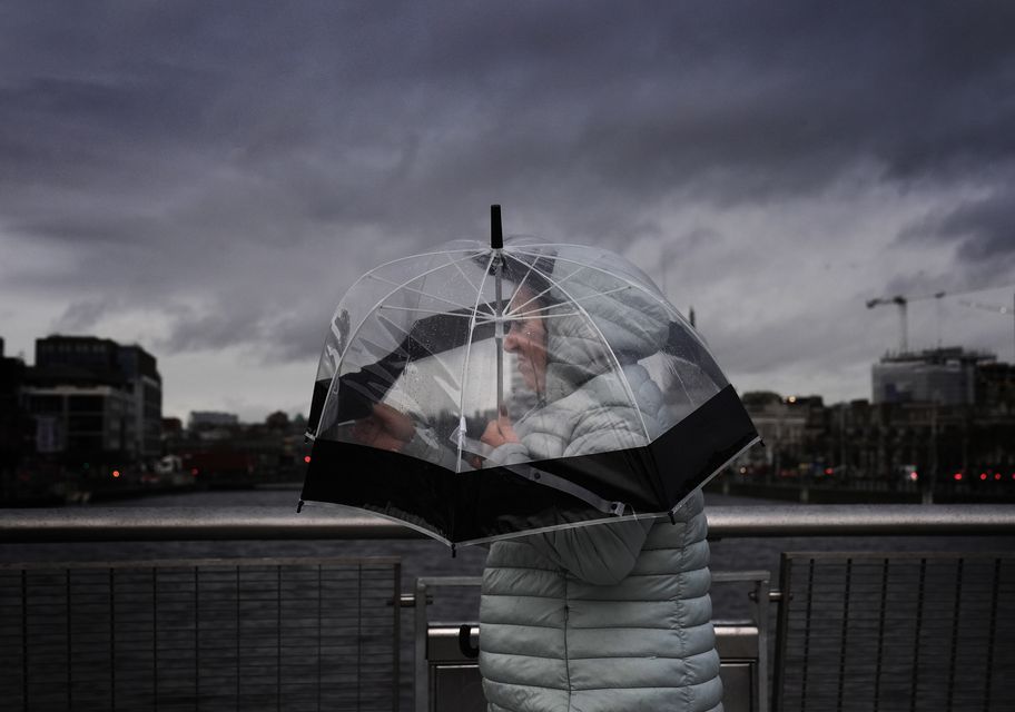 A person takes shelter under an umbrella as they cross the Sean O’Casey Bridge in Dublin city centre ahead of Storm Darragh (Brian Lawless/PA)