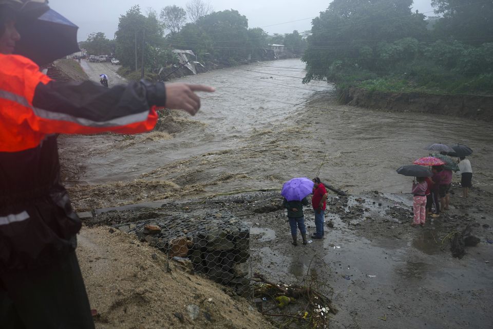 Residents stand alongside the banks of a river on the outskirts of San Pedro Sula, Honduras (Moises Castillo/AP)