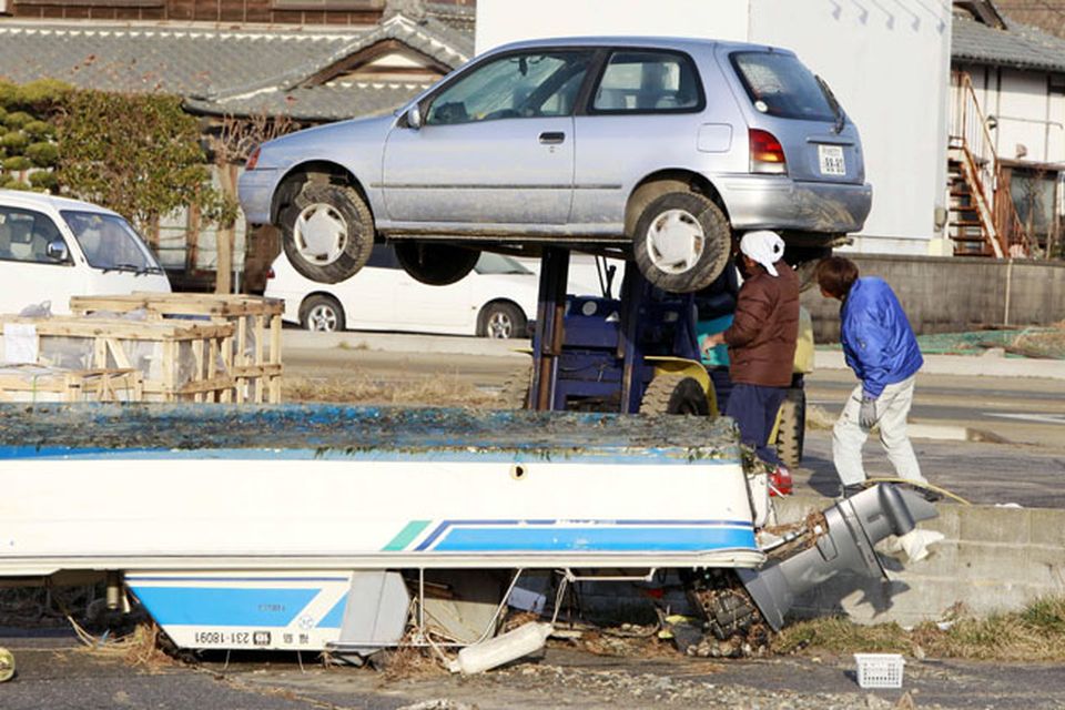 Residents of the seaside town of Yotsukura, northern Japan, inspect under their car as they clear debris from their homes Monday, March 14, 2011, three days after a giant quake and tsunami struck the country's northeastern coast. (AP Photo/Mark Baker)