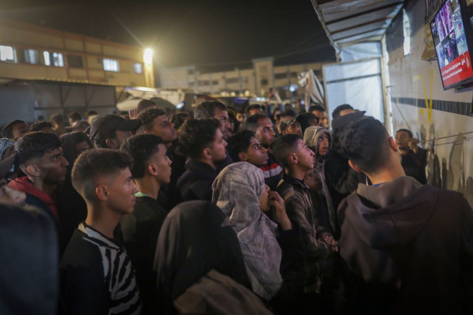 Palestinians watch TV as they await the imminent announcement of a ceasefire deal between Hamas and Israel in Khan Younis, central Gaza (AP Photo)