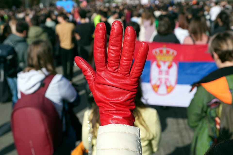 A woman raises a red glove symbolising blood during the student-led 24-hour blockade at an intersection in Belgrade (Darko Vojinovic/AP)