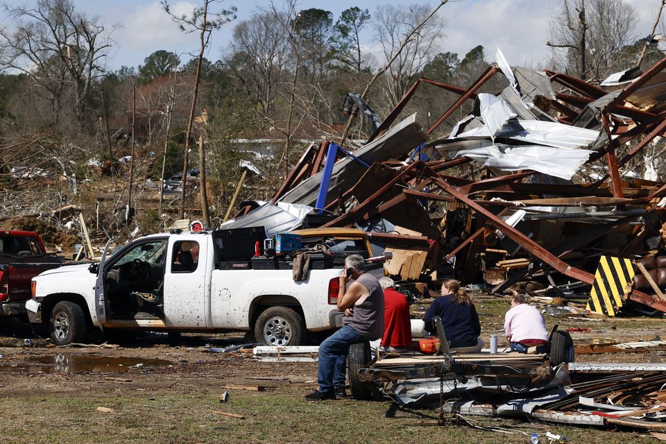 Friends and family members take a break as they search for belongings in the damage after a tornado passed through Plantersville, Alabama (Butch Dill/AP)