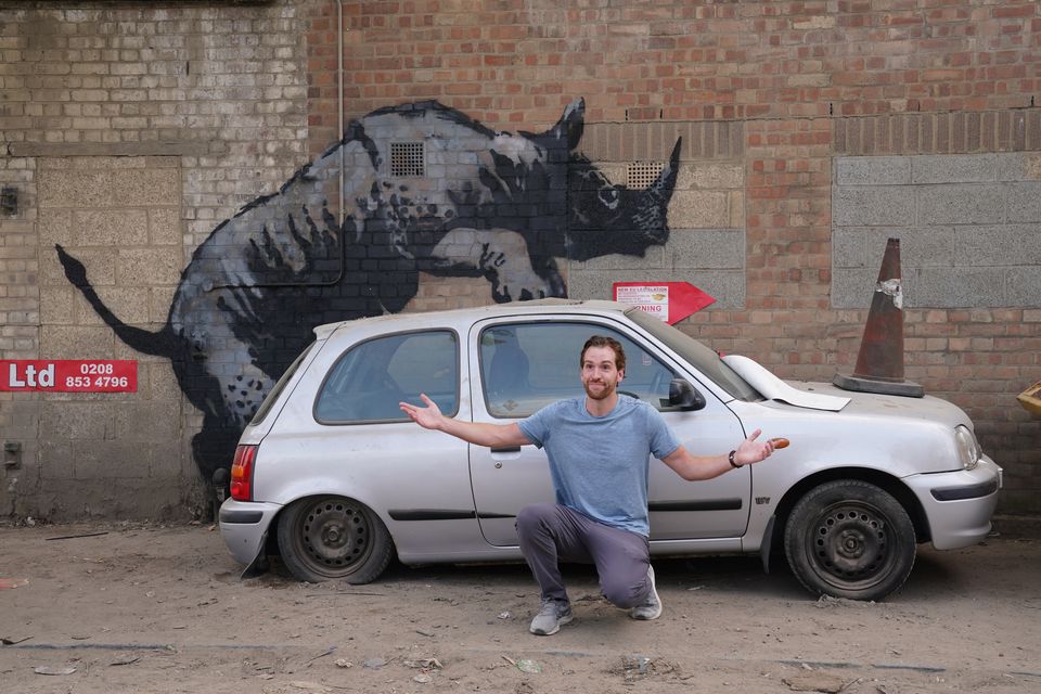 A man poses for a photograph by the new rhino artwork unveiled by Banksy (Lucy North/PA)