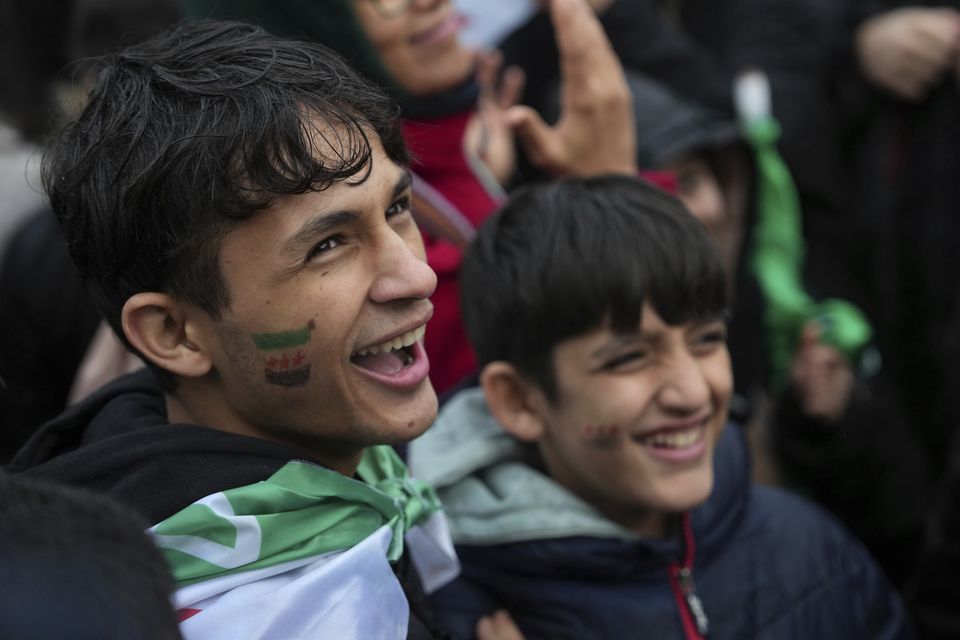 Young Syrians living in France smile during a rally in Paris after the Syrian government fell (Aurelien Morissard/AP)