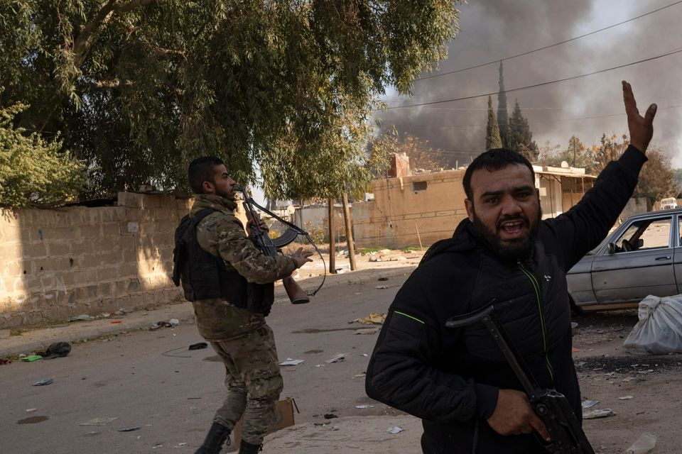 Syrian fighters take position as looters stay inside a building at a residential complex of former Bashar Assad’s military officers in the village of Husseiniyeh (Leo Correa/AP)