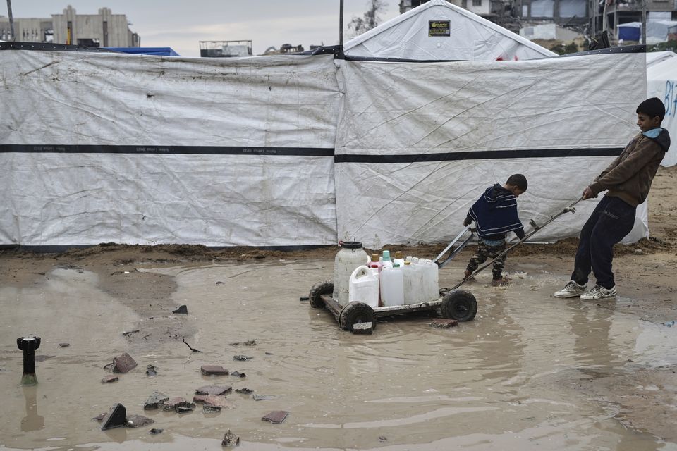 Children carry water in plastic jerrycans at a tent camp for displaced Palestinians in the Zeitoun neighbourhood of Gaza City (Jehad Alshrafi/AP)