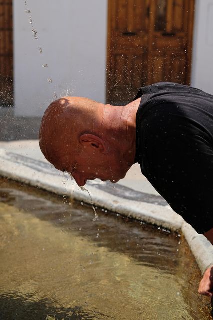 A tourist in Spain cools down at a water fountain (Alamy/PA)