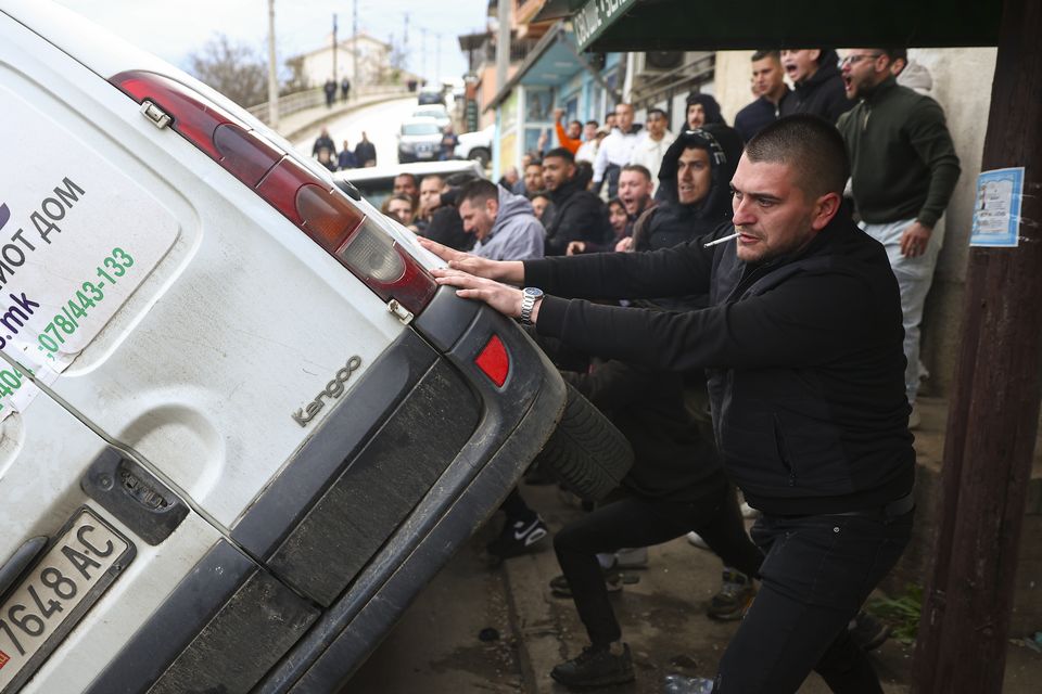 People push a vehicle on its side while protesting near the home of the owner of a nightclub that was the scene of a massive fire in North Macedonia (Armin Durgut/AP)