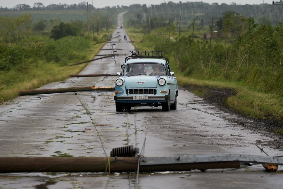 People drive along a road littered with fallen power lines (Ramon Espinosa/AP)