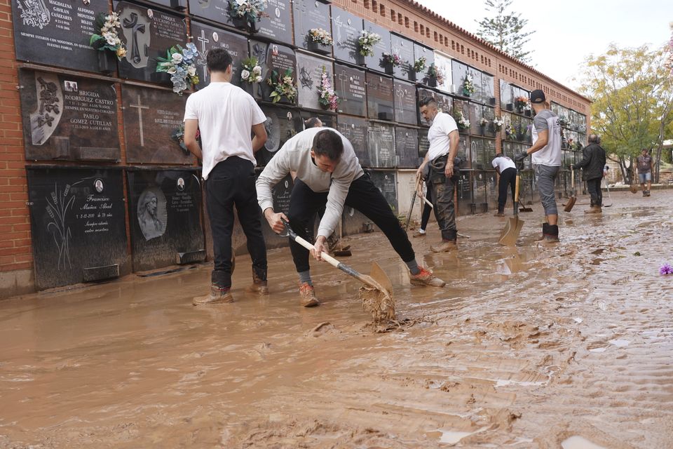 People clear away mud from a flood damaged cemetery on the outskirts of Valencia (Alberto Saiz/AP)