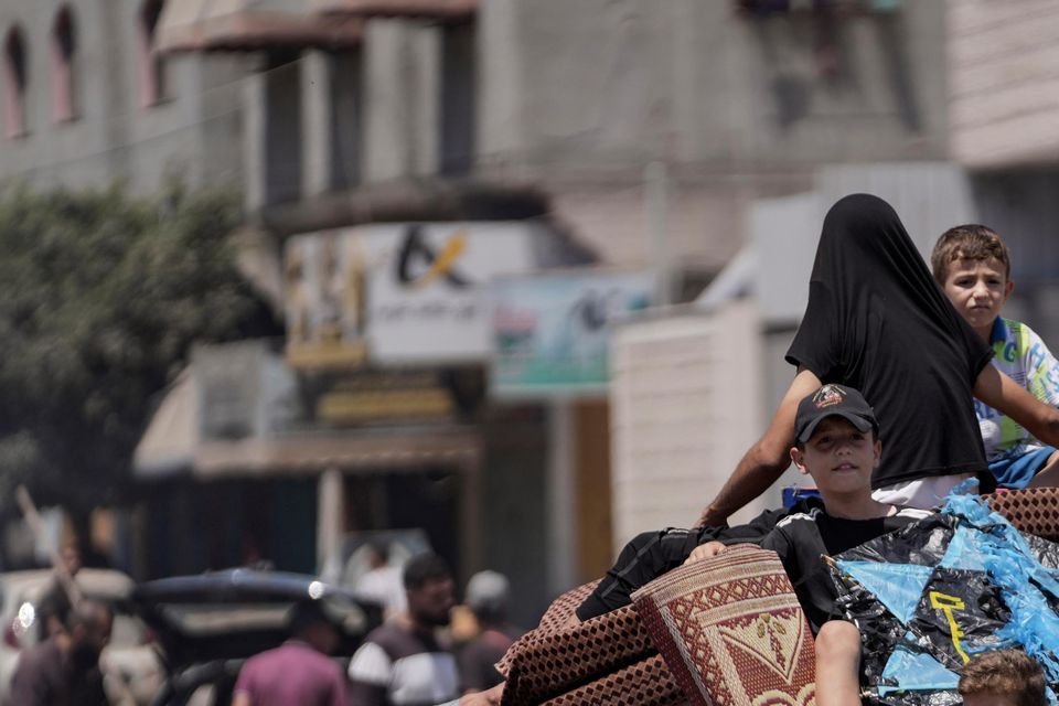 Children sit on a pile of carpets and household belongings in Deir al-Balah (Abdel Kareem Hana/AP)