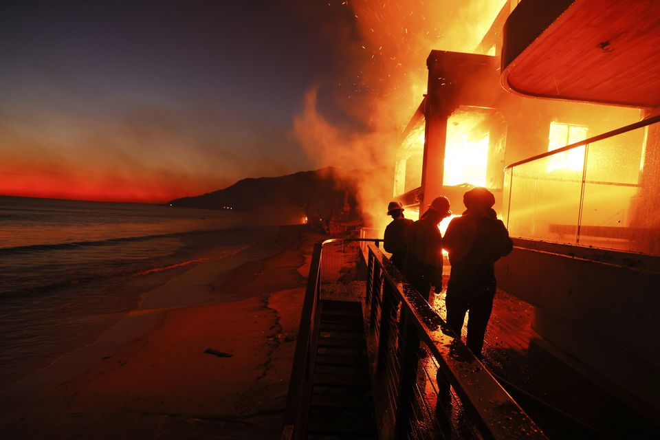 Firefighters work from a deck as the Palisades Fire burns a beachfront property in Malibu (Etienne Laurent/AP)