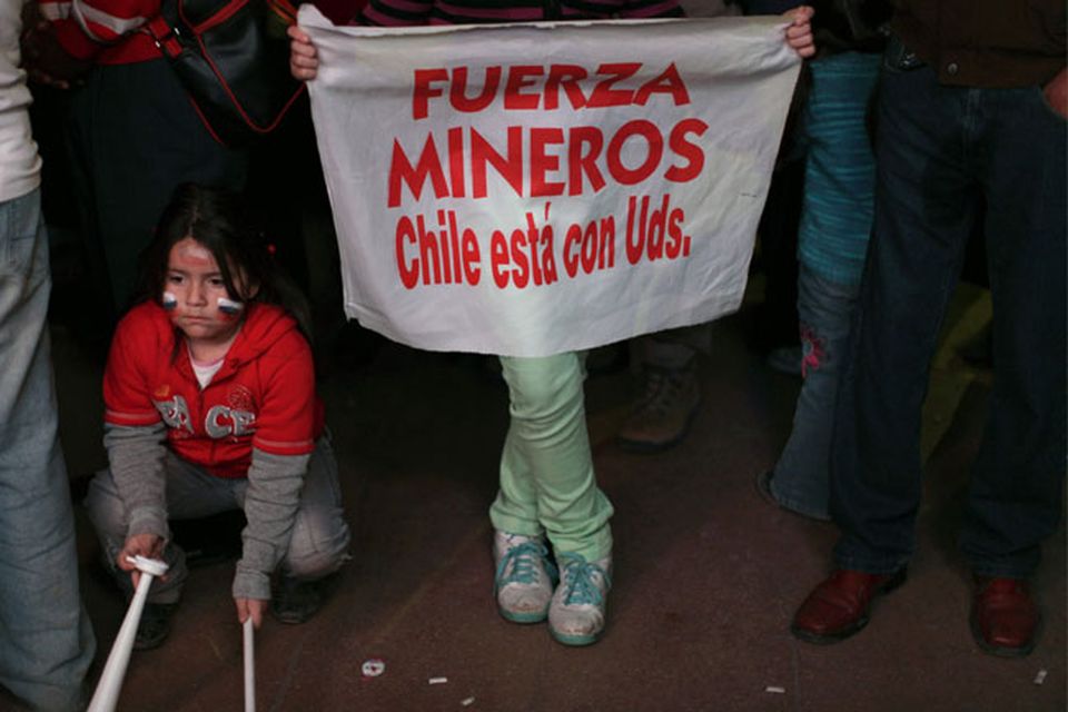A person holds a sign that reads in Spanish "Strength miners, Chile is with you" with a group of people watching on rescue operations on TV taking place at the San Jose mine to free 33 trapped miners, in Copiapo, Chile, late Tuesday Oct. 12, 2010.  Thirty-three miners became trapped when the gold and copper mine collapsed on Aug. 5. (AP Photo/Dario Lopez-Mills)