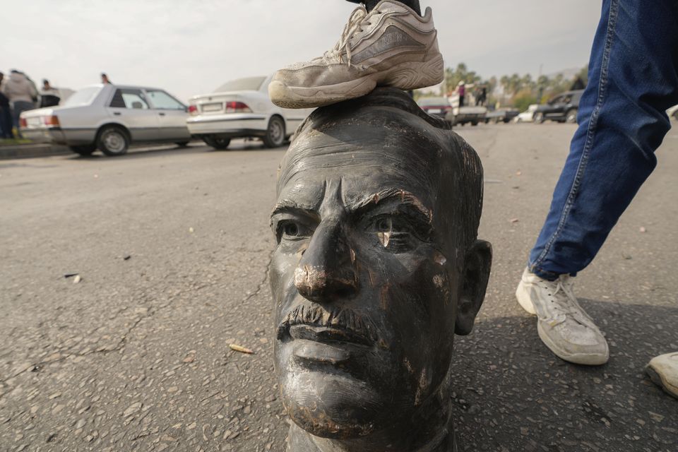 An opposition fighter steps on a broken bust of the late Syrian president Hafez Assad in Damascus following the downfall of the government of his son Bashar (Hussein Malla/AP)